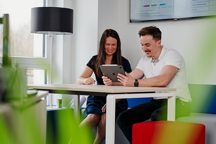 zwei Personen sitzen nebeneinander am Tisch und schauen auf ein Tablet