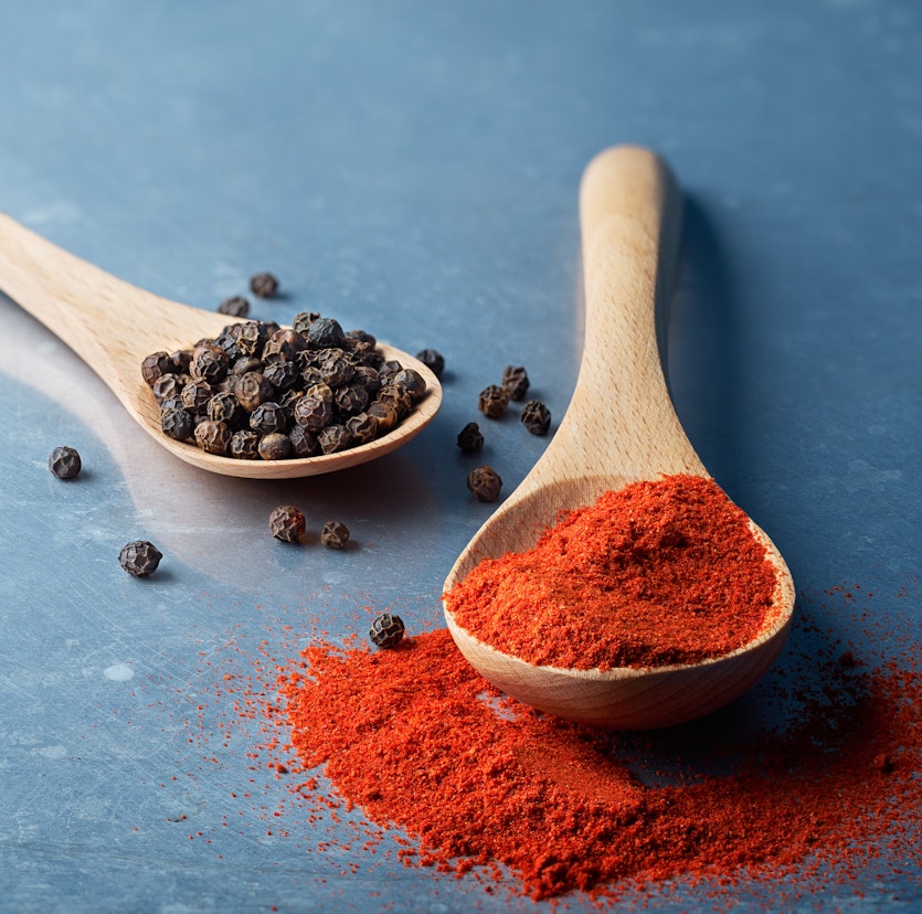Holzlöffel mit rotem Paprikapulver und Schwarzem Pfeffer auf blauem Tisch