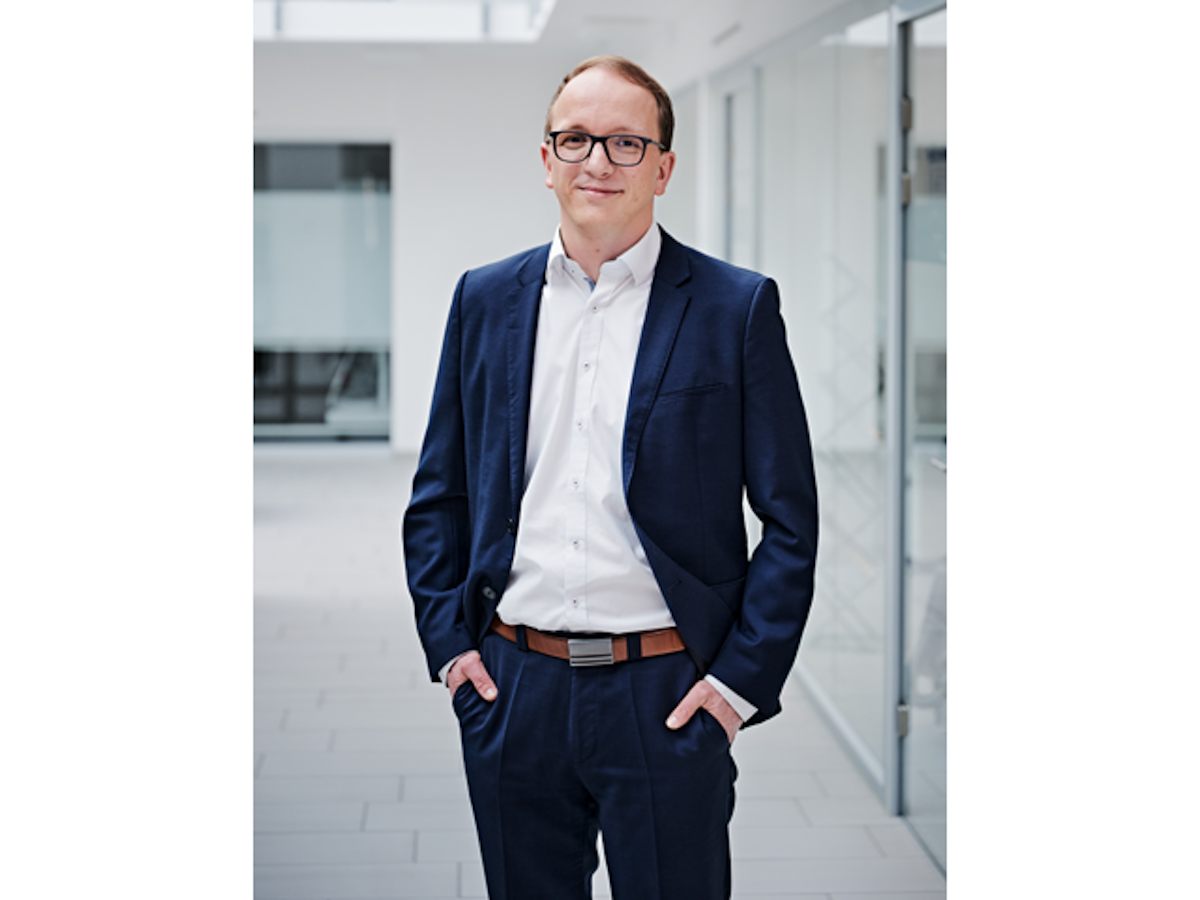 Junger Mann mit Brille und blauem Anzug schaut in die Kamera