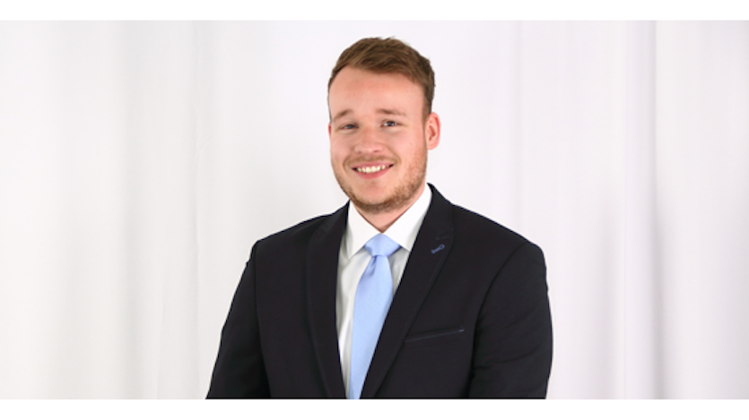 Junger lächelnder Mann mit dunklem Jacket und hellblauer Krawatte