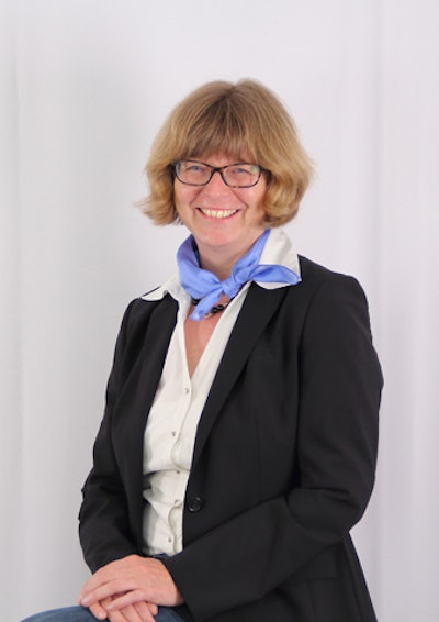 Frau mit Blouson, blauem Halstuch und Brille lächelt sitzend