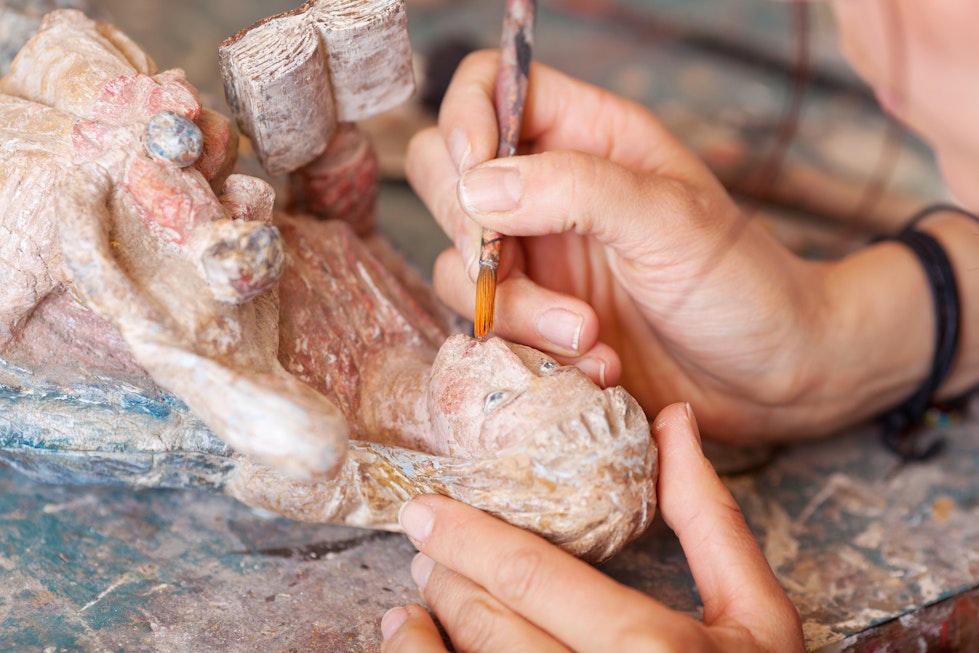 Restaurierungsarbeiten an einer Holzfigur mit einem Pinsel