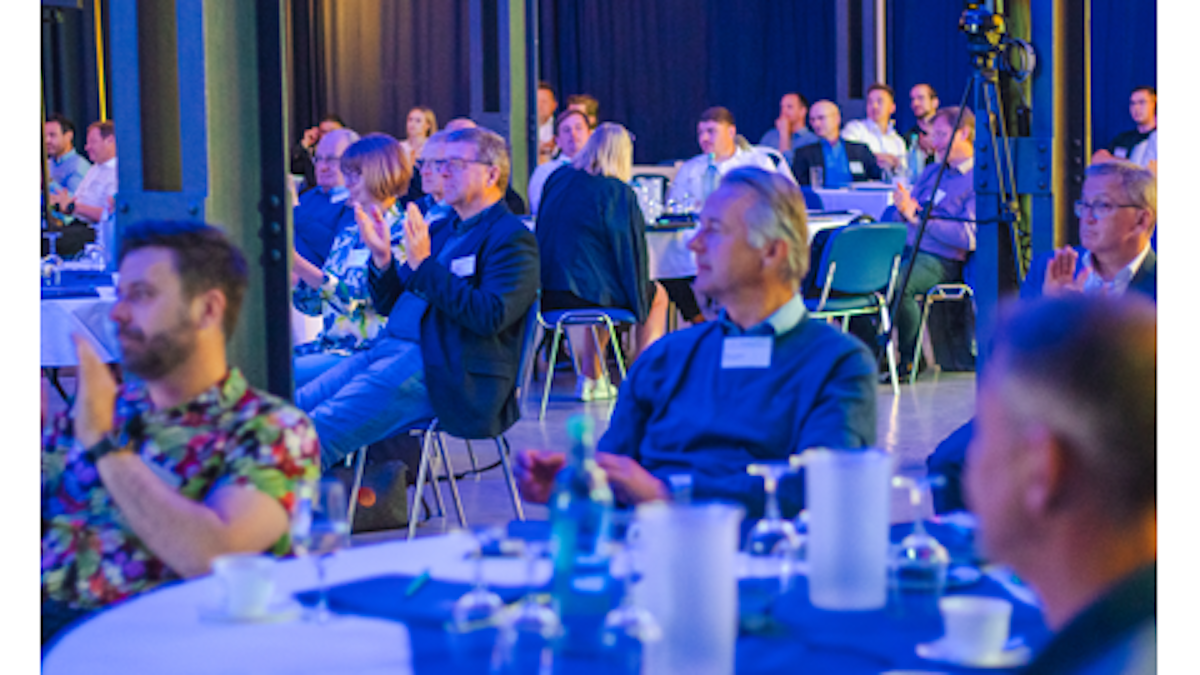 Menschen sitzen an einem Tisch herum und hören einen Vortrag