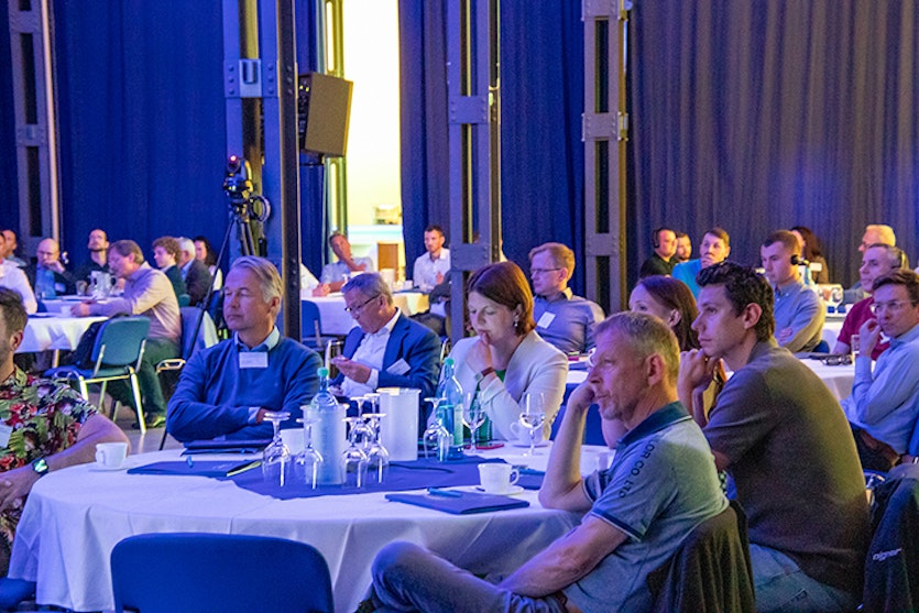 Mehrere Männer & Frauen sitzen bei einer Tagung und lauschen