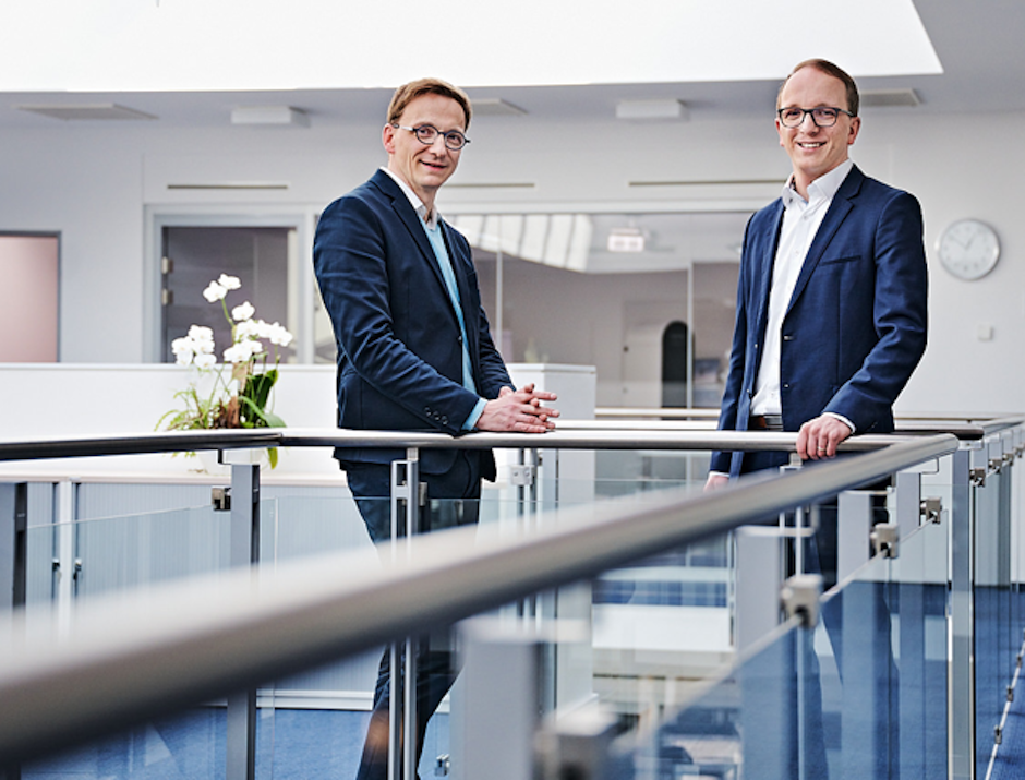 Zwei junge Männer in Jackets lächeln in die Kamera